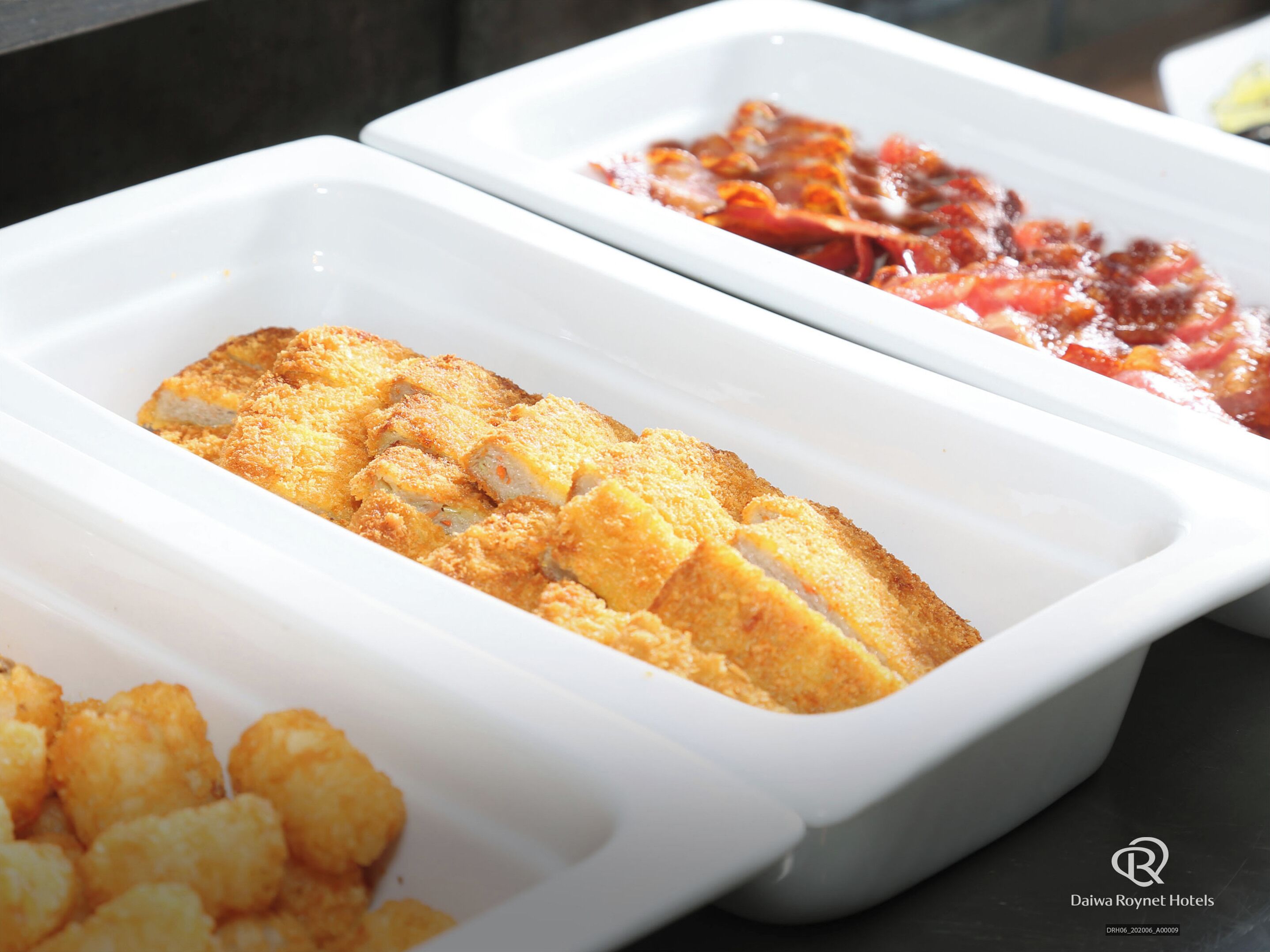 A buffet with various dishes including breaded fish, tater tots, and a tomato-based dish.