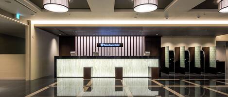 A modern hotel reception area with a check-in counter, a digital display, and a waiting area with privacy screens.