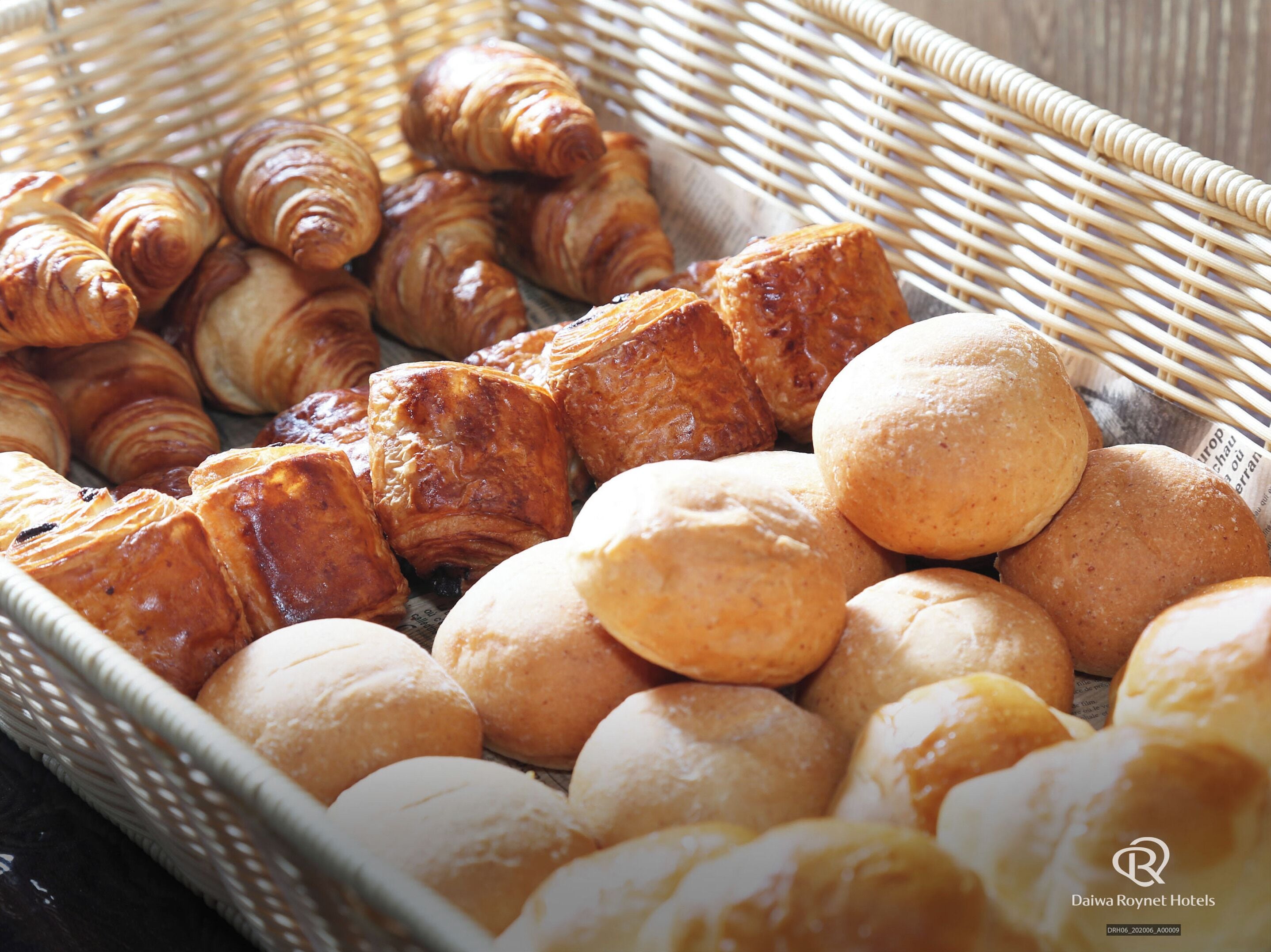 A wicker basket filled with various baked goods, including croissants and round bread rolls.