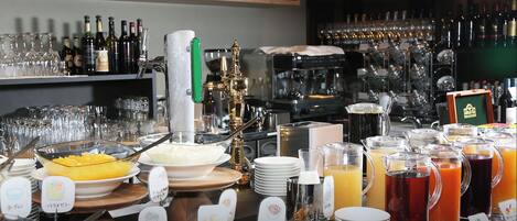 A buffet setup with various food items and beverages, including a coffee machine and a wine rack in the background.
