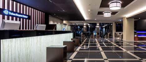 A modern hotel lobby with a reception desk, seating area, and a check-in counter.