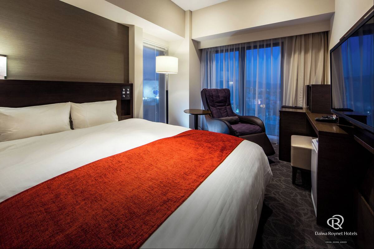 Habitación de hotel con una cama grande, un escritorio, una silla y un televisor.