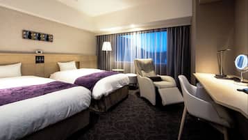 A hotel room with two beds, a desk, a chair, a lamp, and a window with curtains.