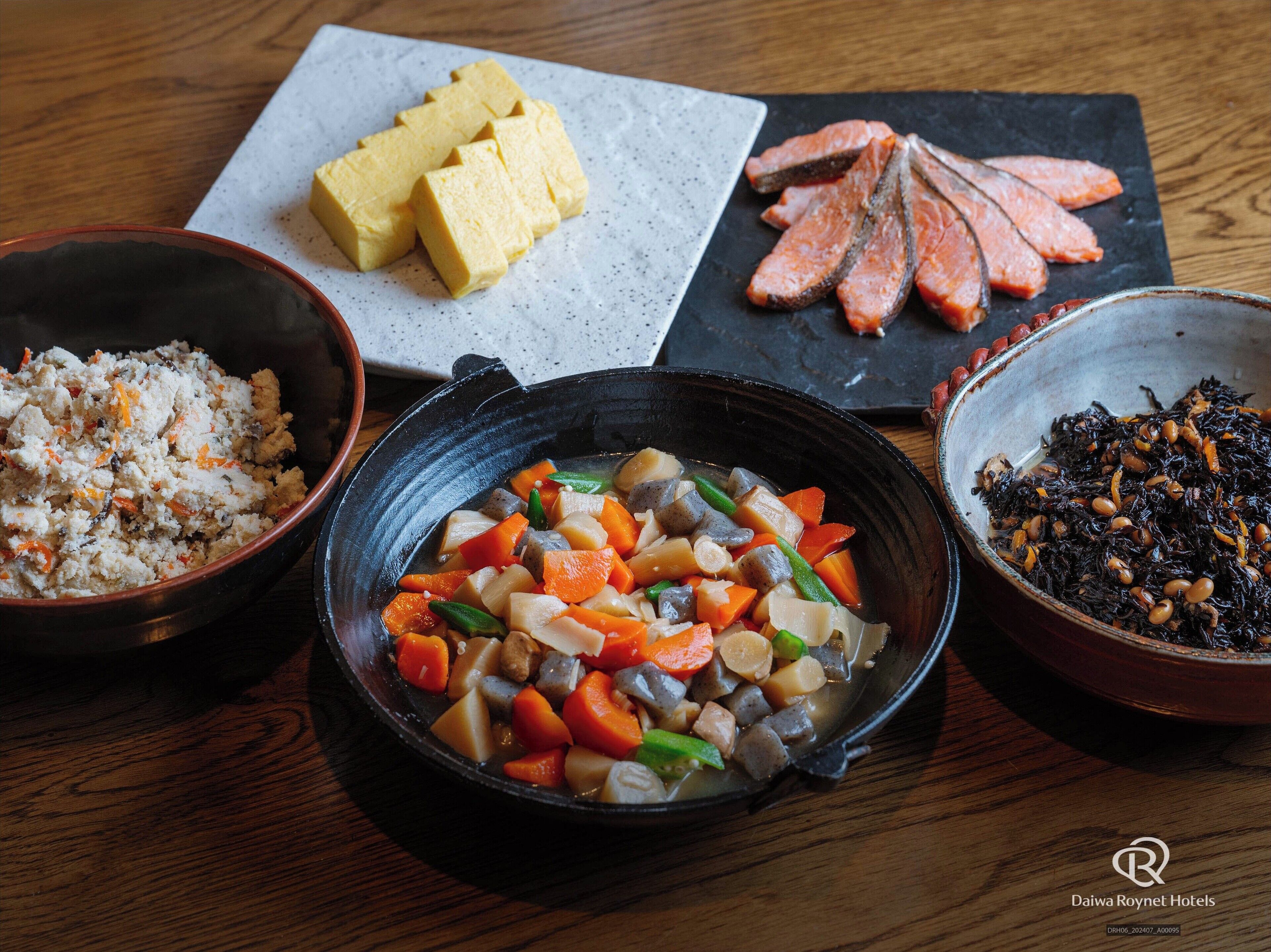 Una mesa con diferentes platos, incluyendo tofu, salmón y un guiso de verduras.