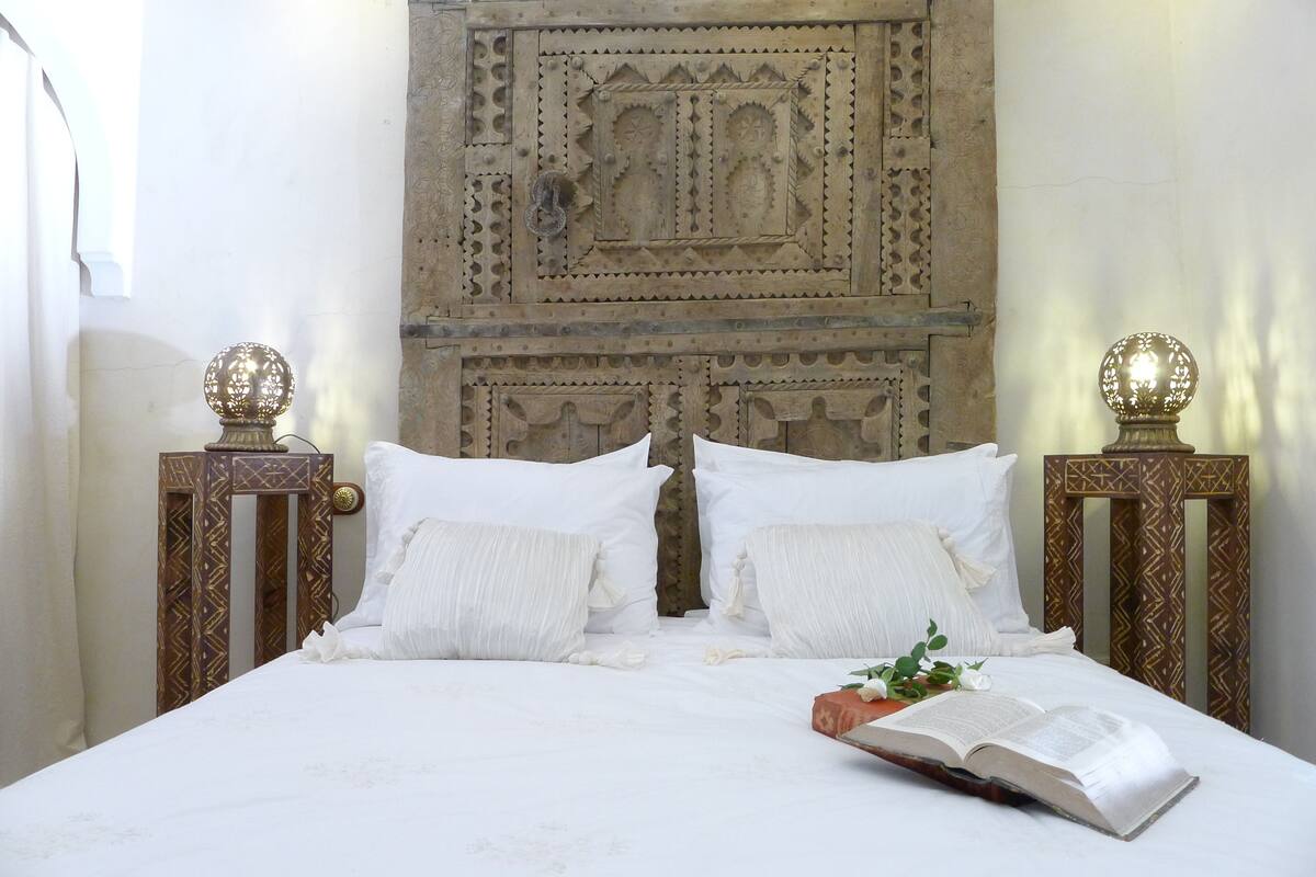 A bed with white linens, two nightstands with decorative lamps, and a carved wall behind the bed.