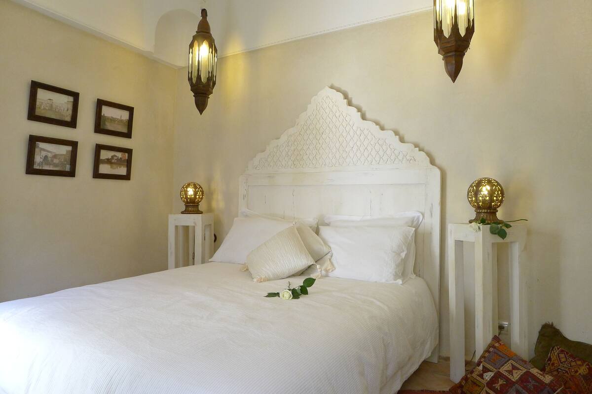 A neatly made bed with white linens, a decorative headboard, and two bedside lamps.