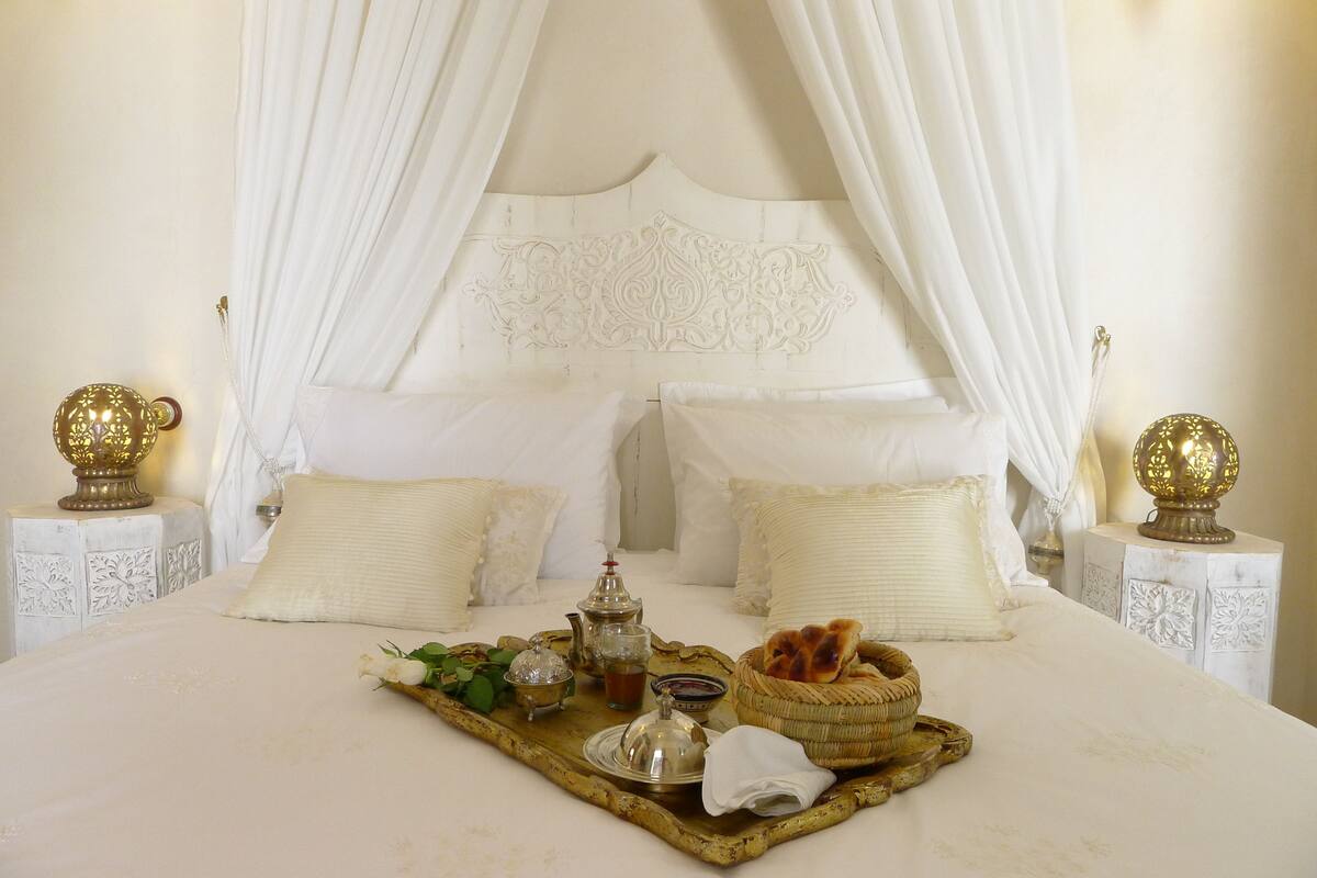 A neatly made bed with white linens, a tray with tea and bread, and decorative lamps on nightstands.