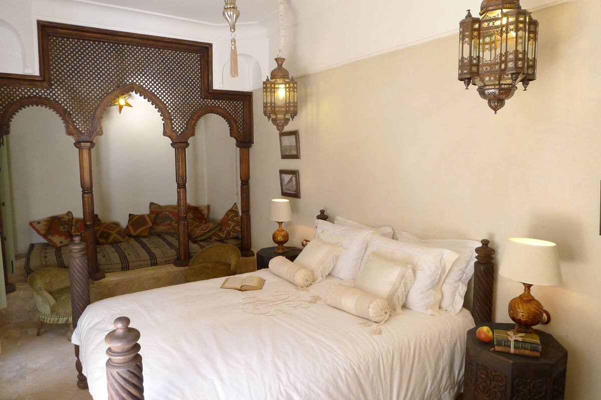A bedroom with a large bed, ornate wooden headboard, a decorative mirror, and a hanging lantern.