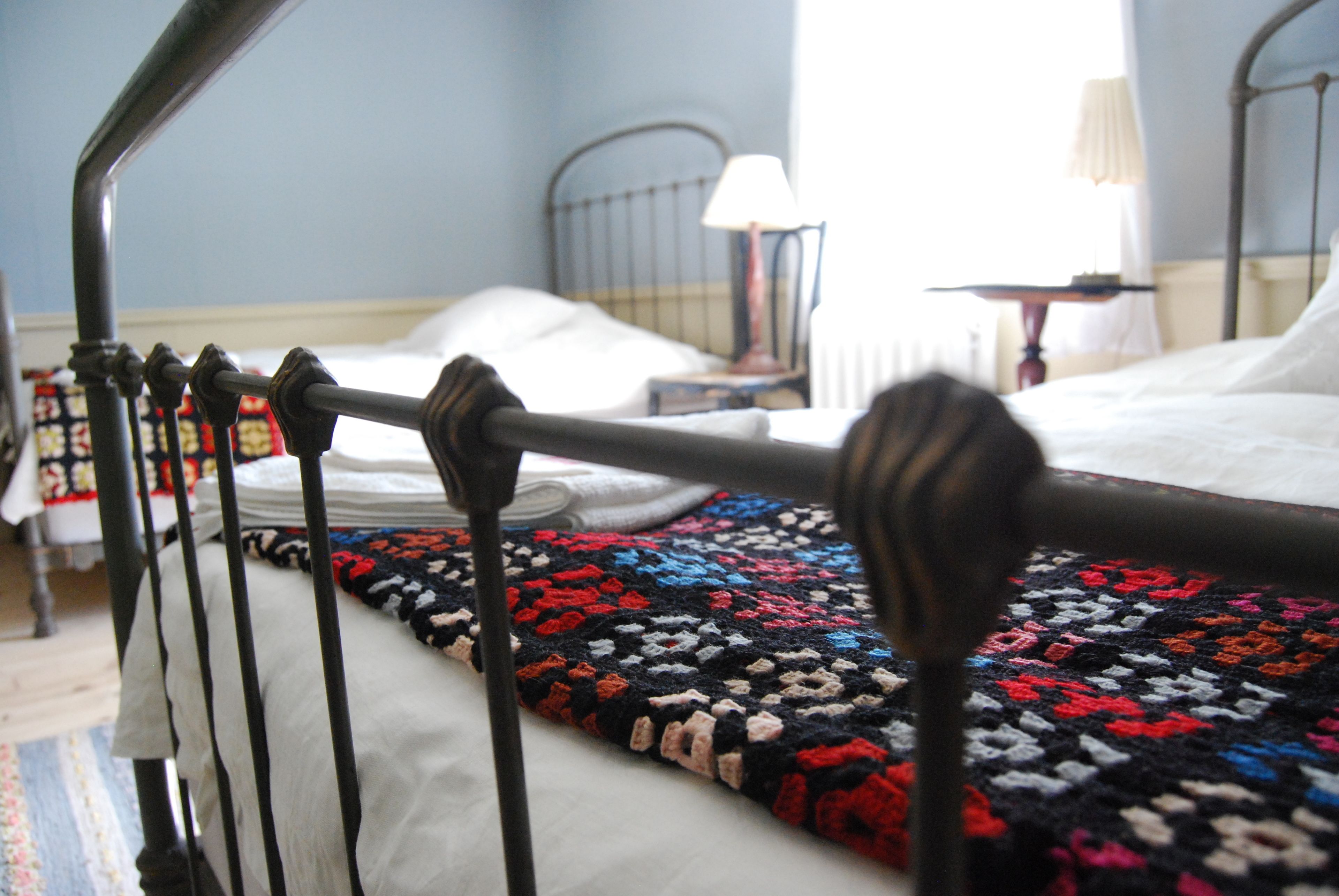 A bed with a colorful blanket, a metal headboard, and a bedside table with a lamp.