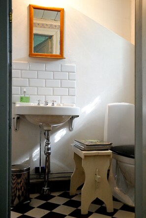 Une salle de bain avec un lavabo blanc, un miroir et un petit tabouret en bois.