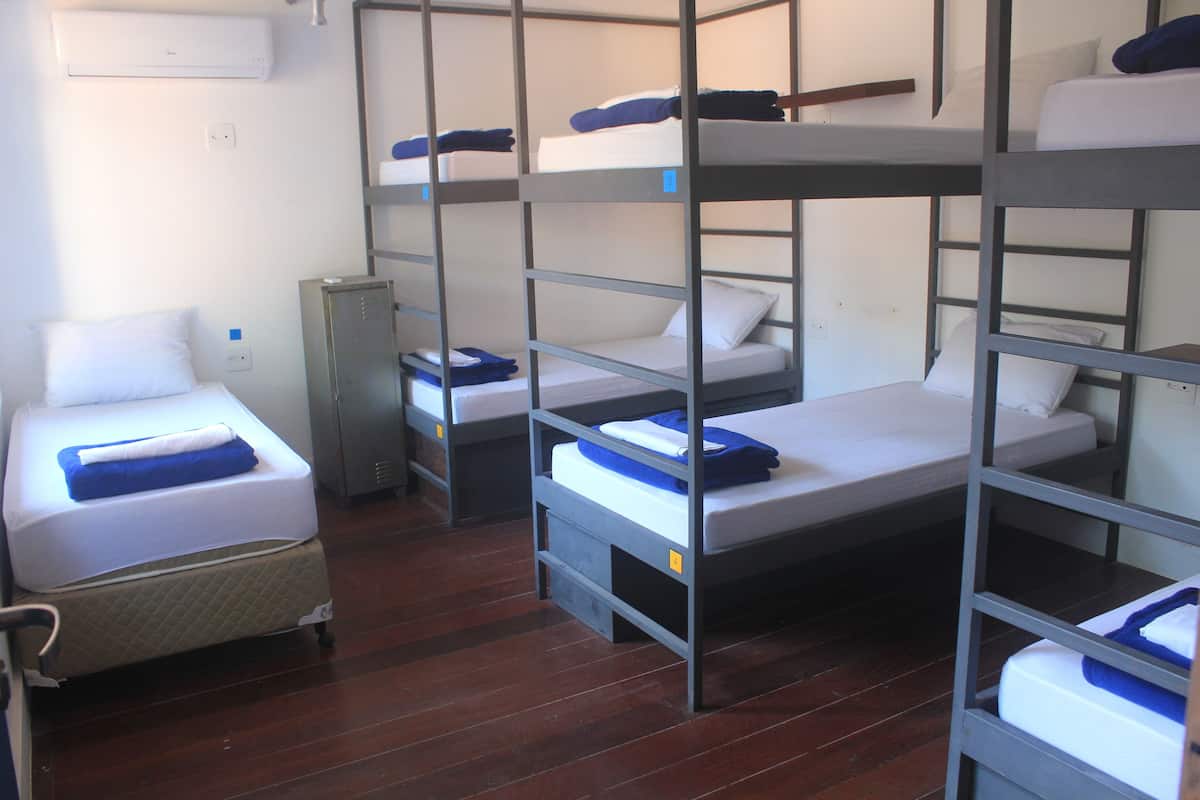 A dormitory room with bunk beds, a small cabinet, and a mattress on wheels.