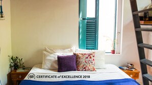 Una cama bien hecha con un edredón azul, almohadas blancas y un certificado de excelencia sobre el cubrecolchón.