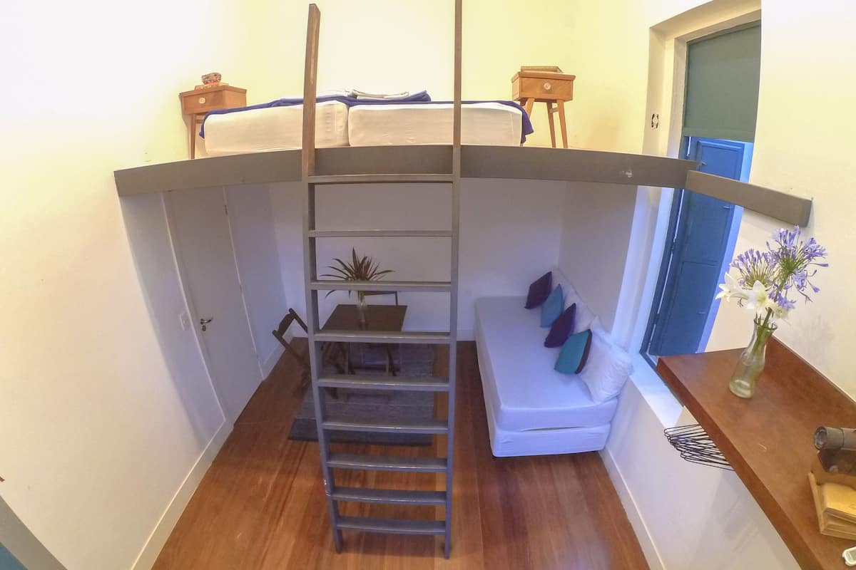 A compact room with a bunk bed, a small table, a chair, a sofa, and a vase with flowers.