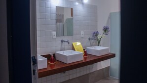 Un baño moderno con dos lavamanos blancos, un espejo grande y un florero con flores.