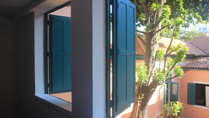 Una habitación con ventana que da a un árbol y un edificio con tejado de tejas.