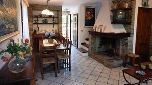 A dining area with a table and chairs, a fireplace, and a kitchen area with shelves.