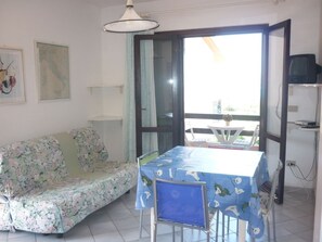 A room with a floral sofa, a table with a blue tablecloth, a ceiling light, and a view through a glass door. - AbitaSardegna Stintino (Stintino)