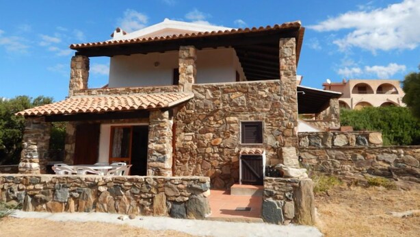 A two-story stone house with a tiled roof, a stone porch, and a small outdoor seating area. - AbitaSardegna Pittulongu (Olbia)