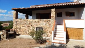 A stone-clad building with a tiled roof, a staircase leading to a covered porch, and a small garden area. - AbitaSardegna Pittulongu (Olbia)