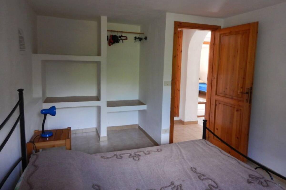 A bedroom with a bed, a nightstand, a wooden wardrobe, and built-in shelving.