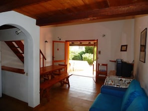Uma sala de estar ampla com um banco de madeira, um sofá azul e uma televisão. Uma escada de madeira leva a um andar superior.