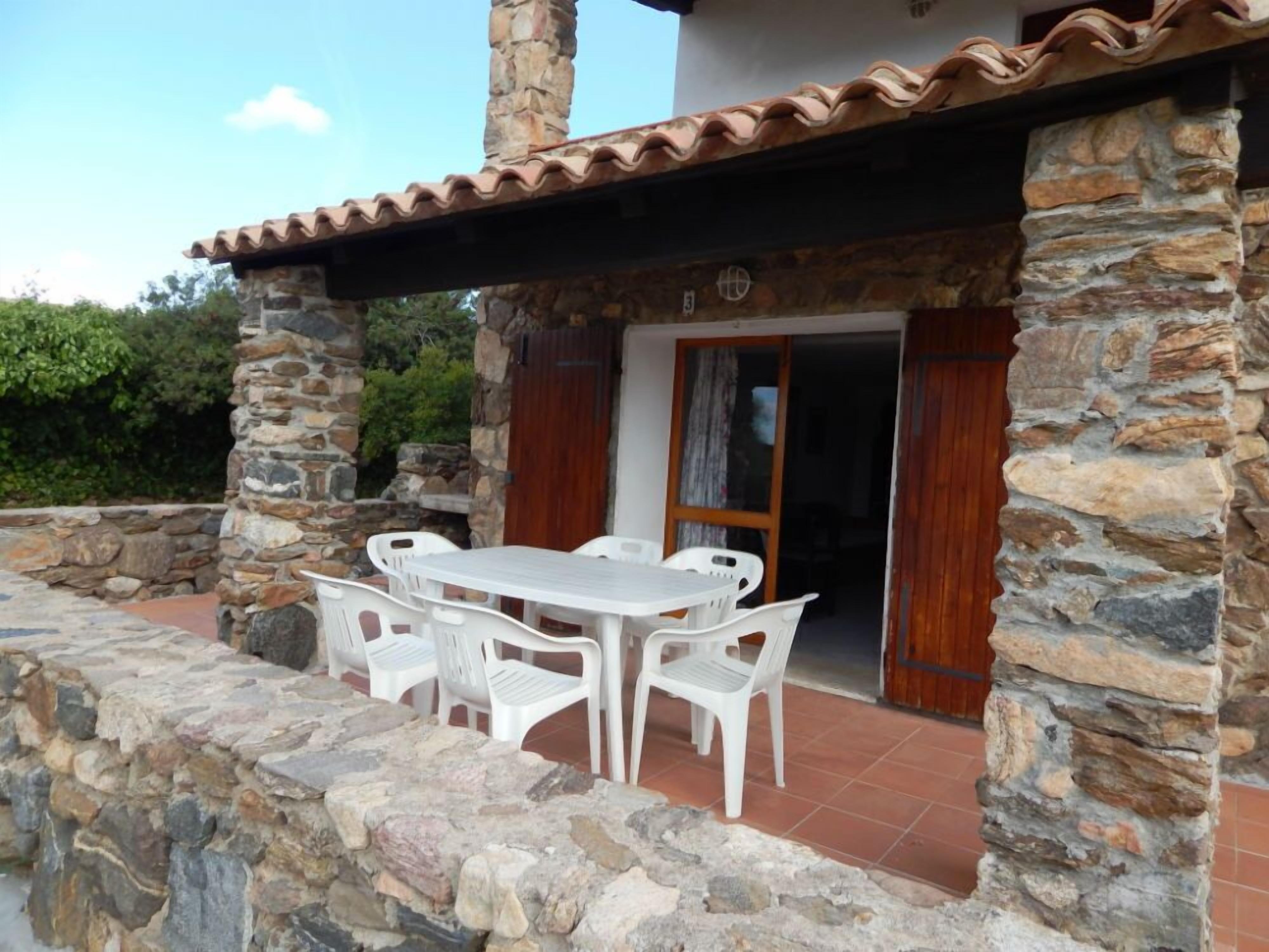 A stone building with a tiled roof, a patio with a table and chairs, and a wooden door.