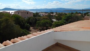 A terrace with terracotta tiles, overlooking a coastal area with buildings and greenery. - AbitaSardegna Pittulongu (Olbia)