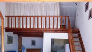 A loft-style room with a wooden staircase, a dining table, a blue sofa, and a kitchen area. - AbitaSardegna Pittulongu (Olbia)