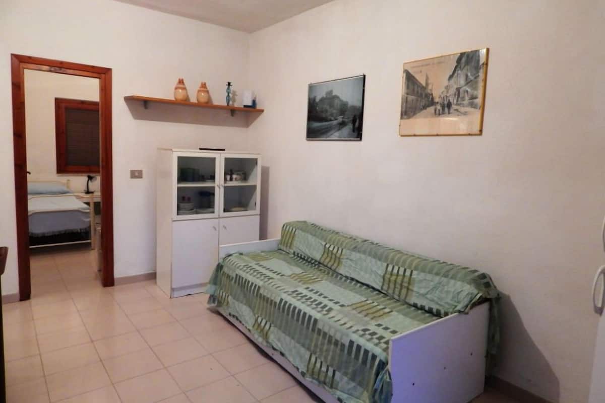 A small room with a sofa, a cabinet, and a bed in the background.
