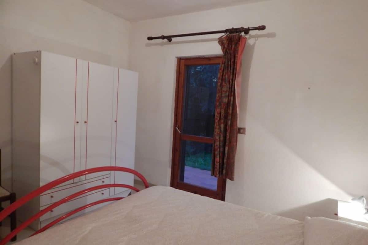 A bedroom with a bed, a wardrobe, a window with curtains, and a red metal bed frame.