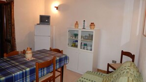 A small, cozy room with a dining table, chairs, a bed, a cabinet with glass doors, and a television on a stand. - AbitaSardegna San Teodoro (San Teodoro)