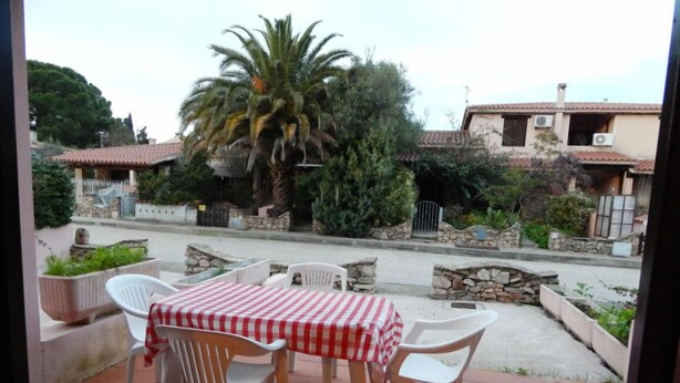 A patio with a table and chairs, a palm tree, and a stone wall. - AbitaSardegna San Teodoro (San Teodoro)
