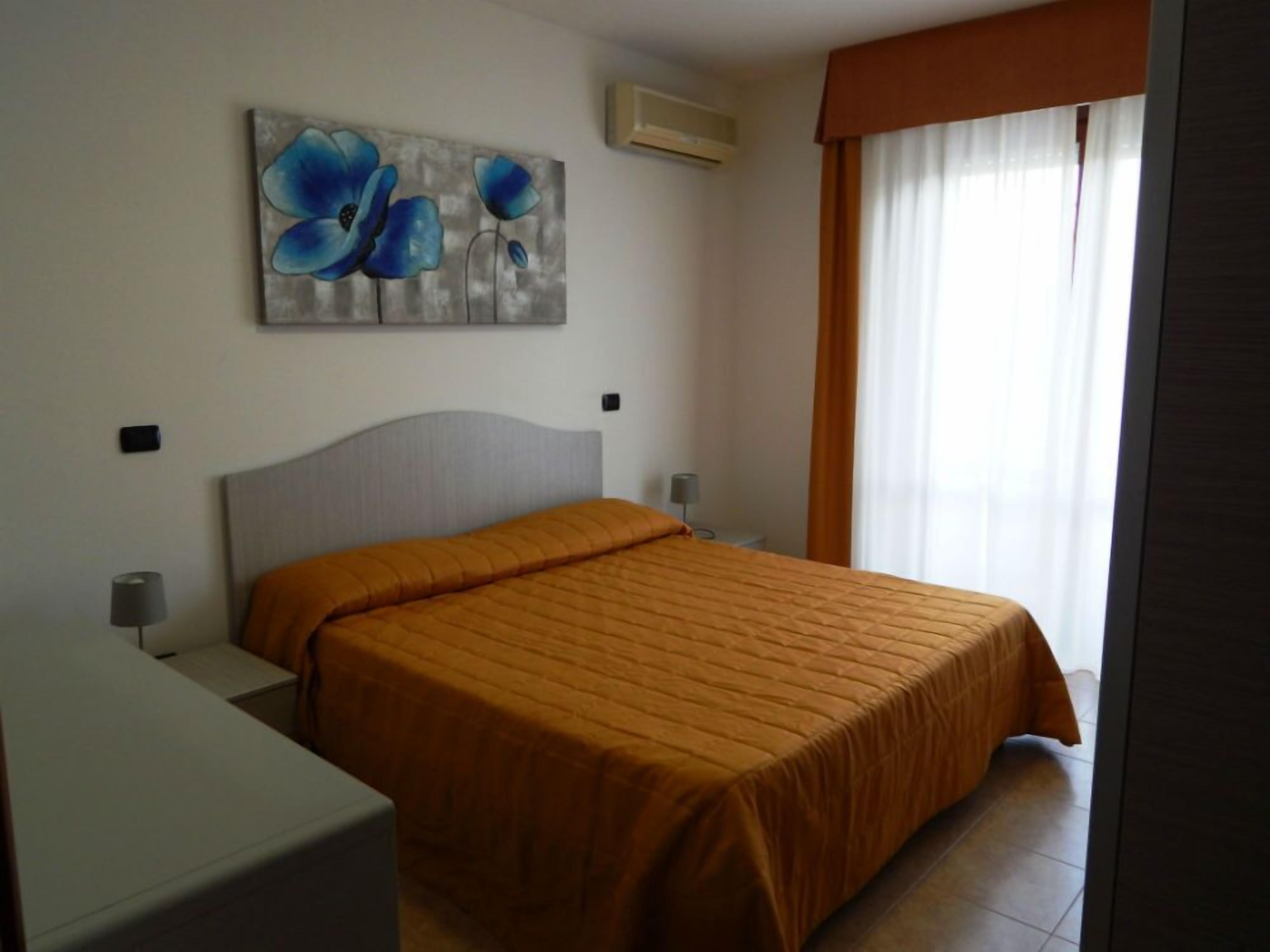 A bedroom with a bed, a nightstand, a lamp, and a painting on the wall.
