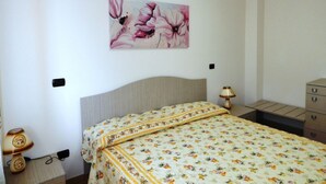 Un dormitorio con cama, una mesita de noche con lámpara, un aparador y un aire acondicionado instalado en la pared.