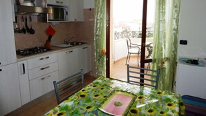 Una cocina compacta con estufa a gas, pileta y muebles blancos. Una mesa de comedor con mantel floral y un centro de mesa rosa se encuentra en el centro.