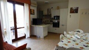 Un espacio habitable compacto con kitchenette, comedor y sofá con cojines naranjas.