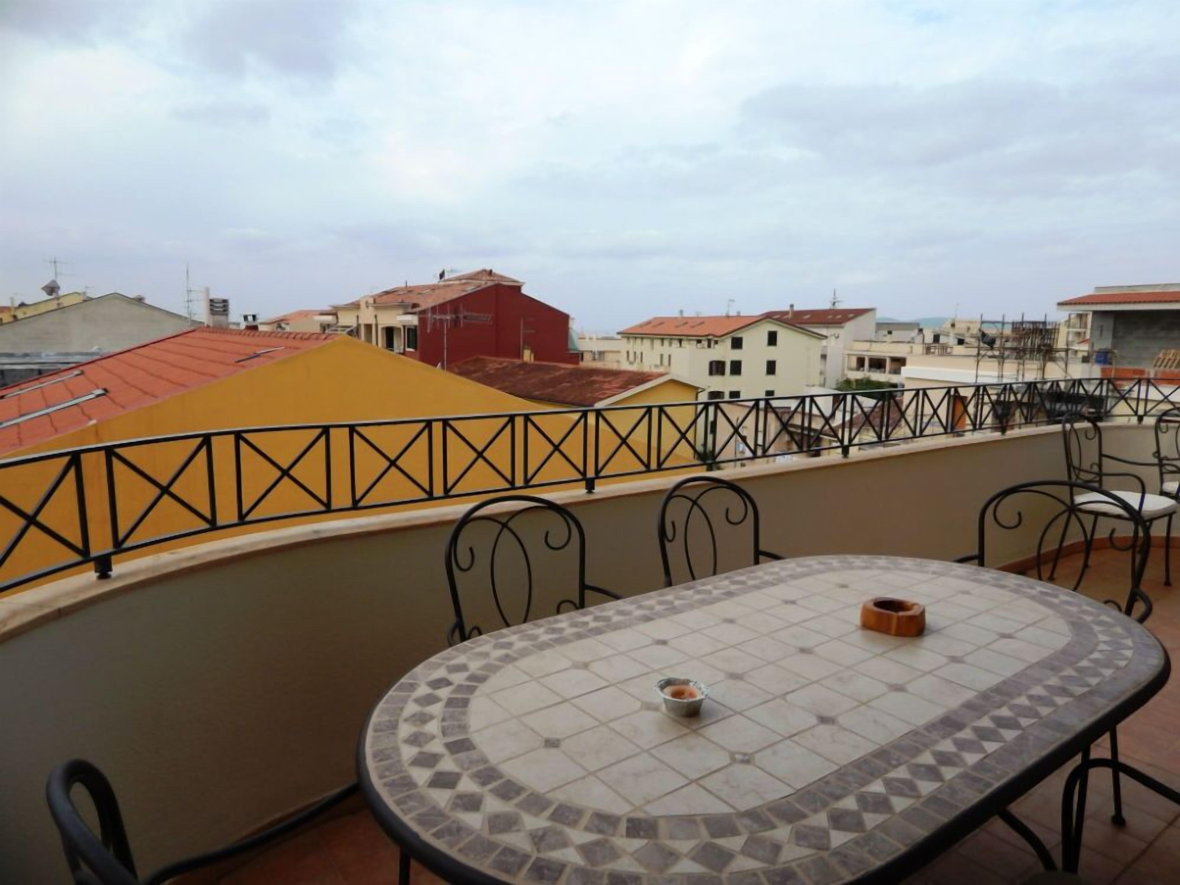 A rooftop terrace with a tiled table and chairs, a metal railing, and a view of surrounding buildings.