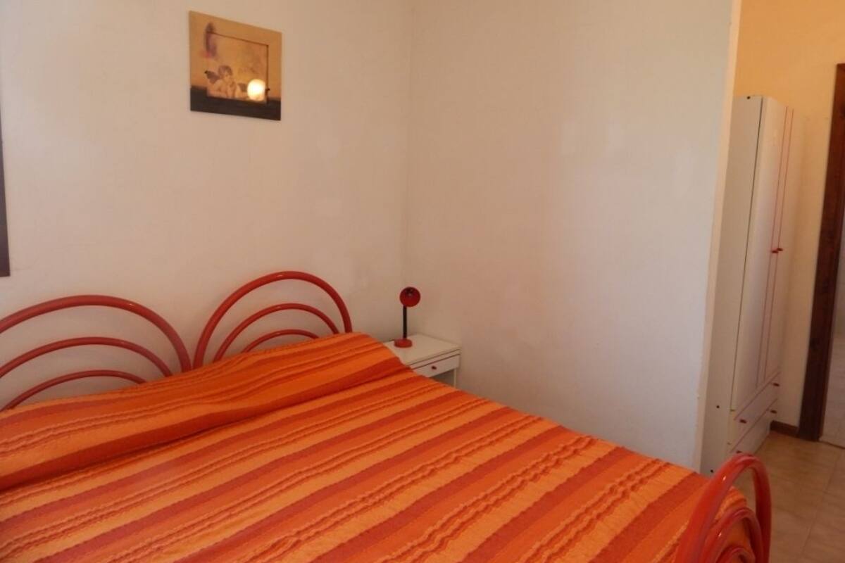 A bedroom with a bed, a nightstand, a wall-mounted picture, and a wardrobe.