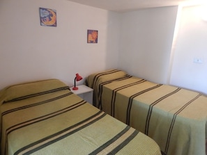 Una habitación con dos camas, cada una con ropa de cama a rayas, una mesita con una lámpara y dos cuadros colgados en la pared.