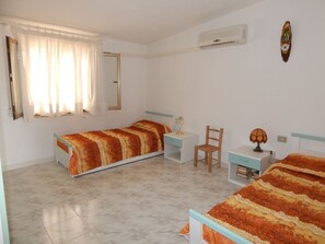 Un dormitorio con dos camas, una silla, una mesita de noche y un aire acondicionado instalado en la pared.