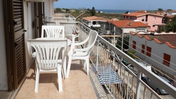 Un balcón con sillas de plástico blanco y una mesa, con vistas a una zona residencial y al mar.