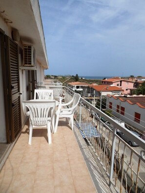 Un balcone con sedie e tavolo in plastica bianca, con vista su una zona residenziale e il mare.