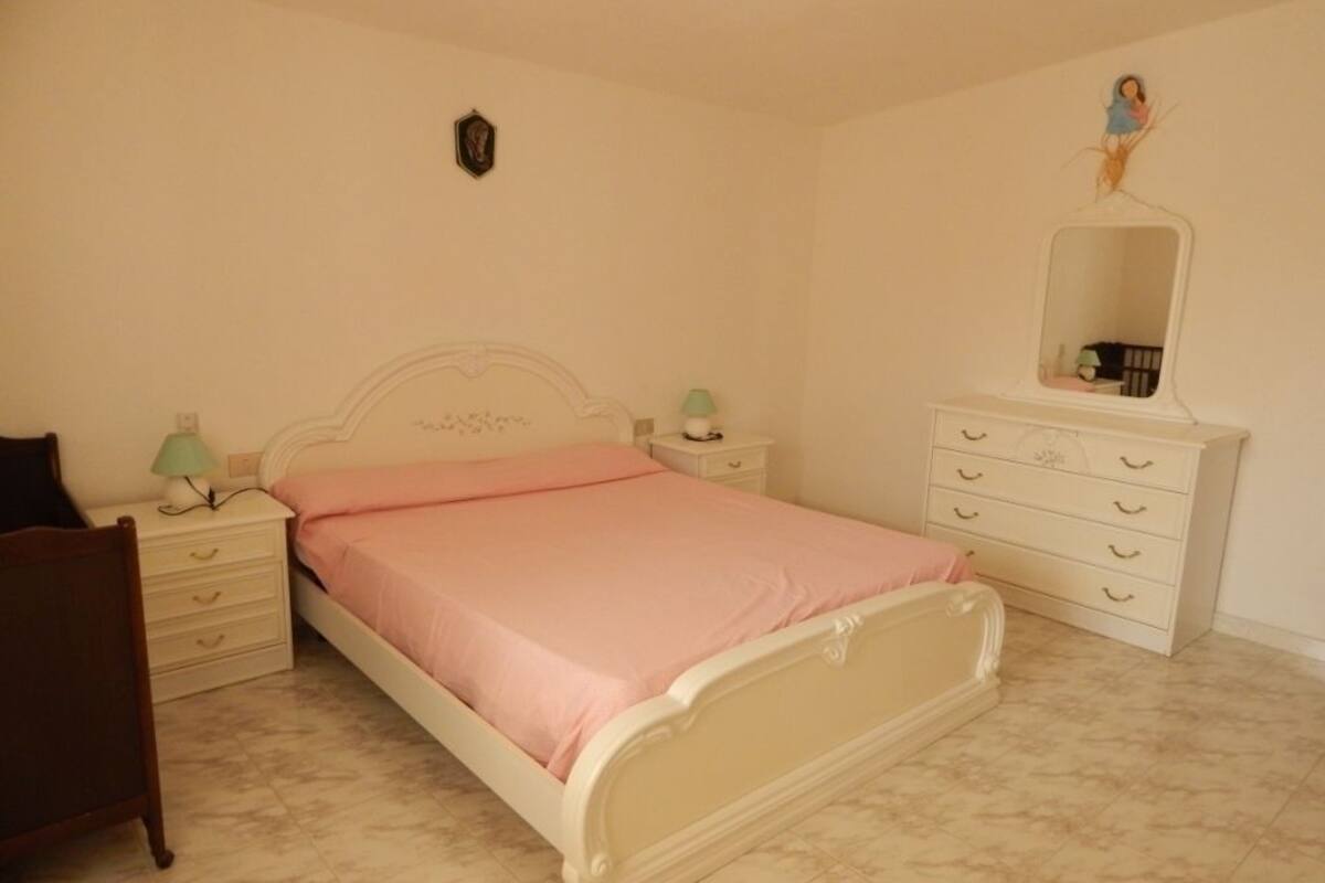 A bedroom with a bed, a dresser, a nightstand, a chair, and a wall-mounted mirror.