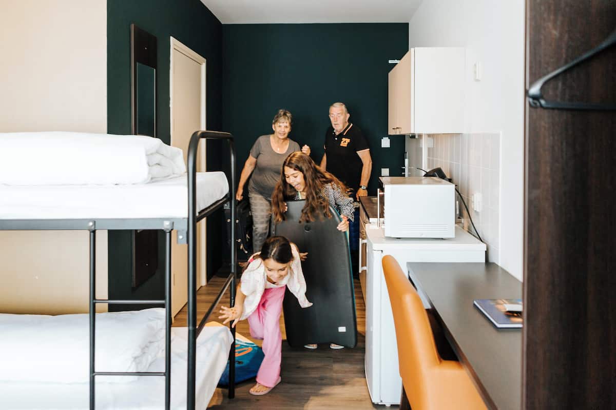 Une chambre d’hôtel avec des lits superposés, un bureau avec un ordinateur et une petite kitchenette.