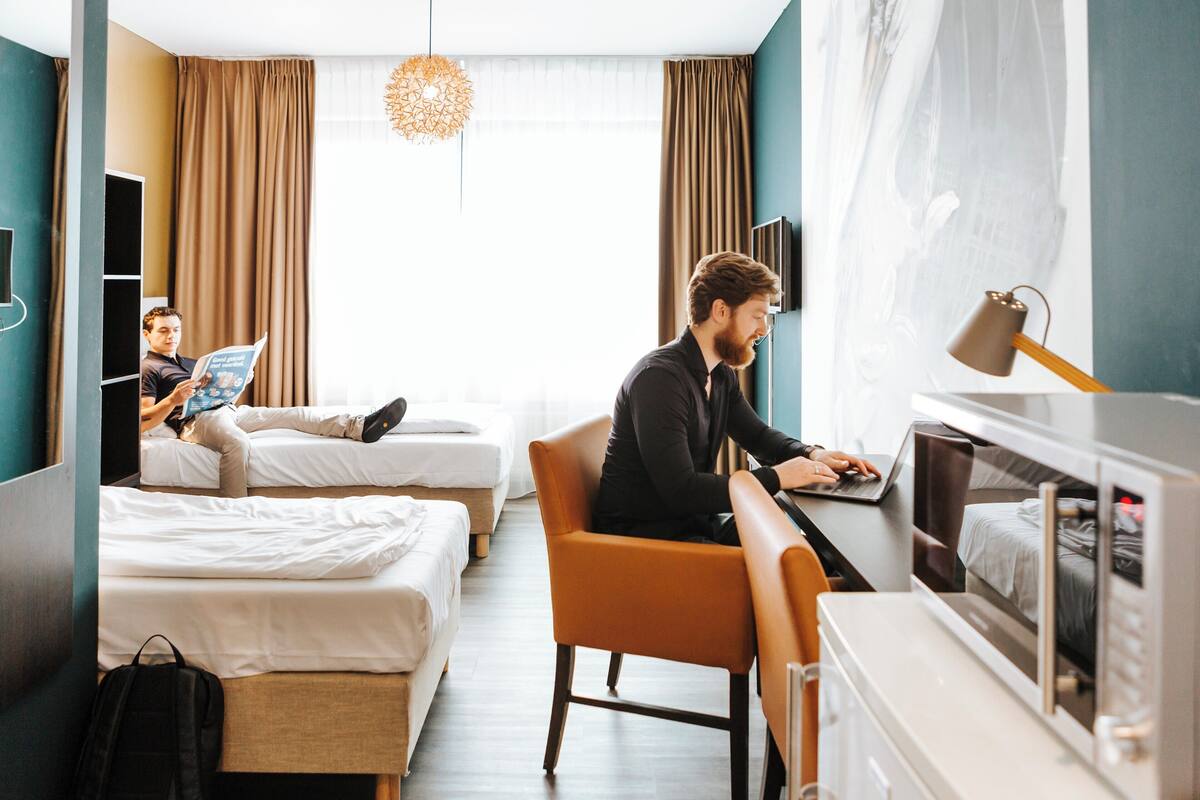 Une chambre d’hôtel avec deux lits, un bureau avec un ordinateur portable et un four à micro-ondes.