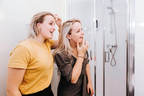 Dos personas en un baño con mampara de cristal y panel de control a la vista.