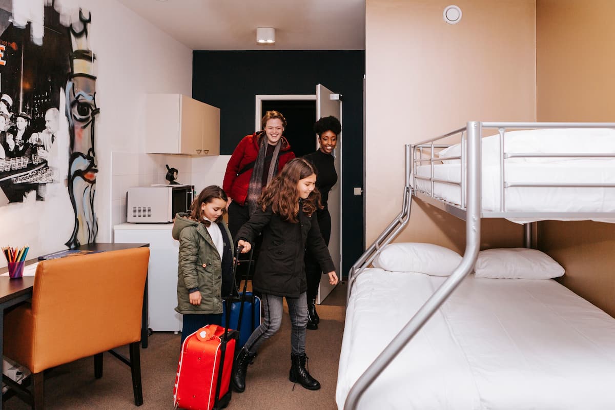 Une chambre avec des lits superposés, un bureau et une chaise. On y trouve également un four à micro-ondes et un petit placard.
