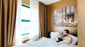 Een hotelkamer met een bed, gordijnen, een raam en een aan de muur hangend schilderij.