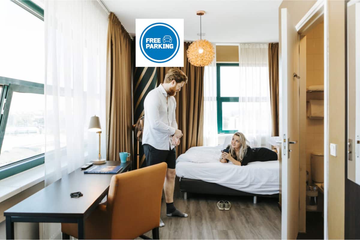 Une chambre d’hôtel équipée d’un lit, d’un bureau, d’une chaise, d’une fenêtre avec des rideaux et d’un panneau indiquant que le stationnement est gratuit.