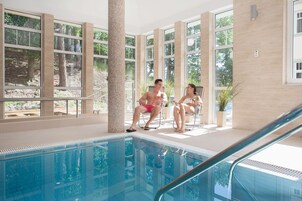 An indoor pool area with large windows, a tiled floor, and a pool with a clear blue water.